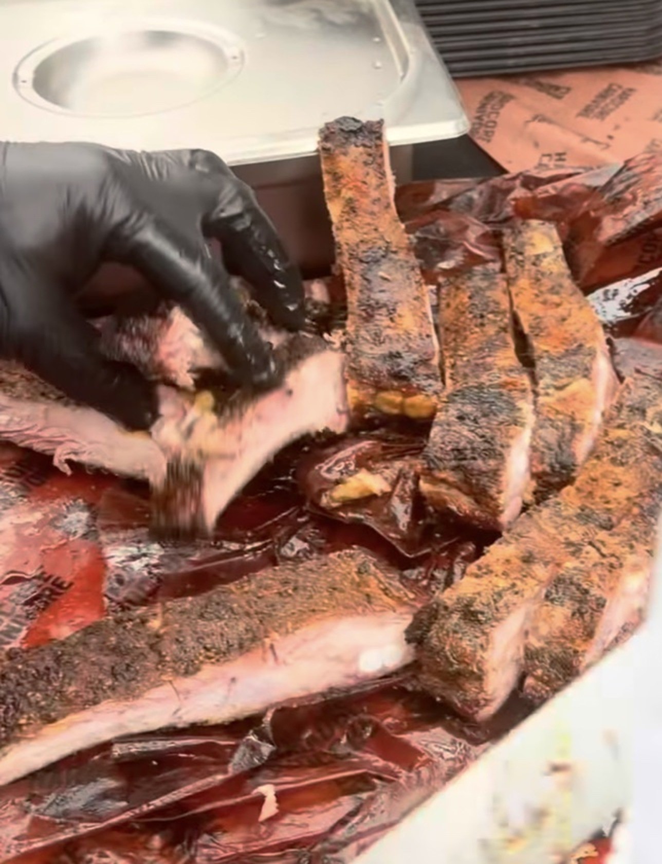 Gloved hands portioning smoked St. Louis ribs on butcher paper at an event